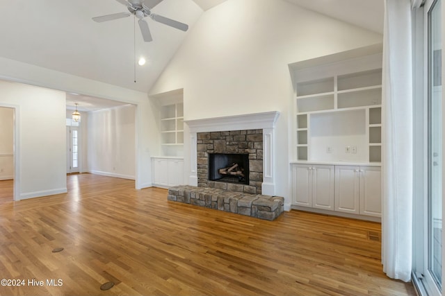 unfurnished living room featuring lofted ceiling, a stone fireplace, built in shelves, ceiling fan, and light wood-type flooring