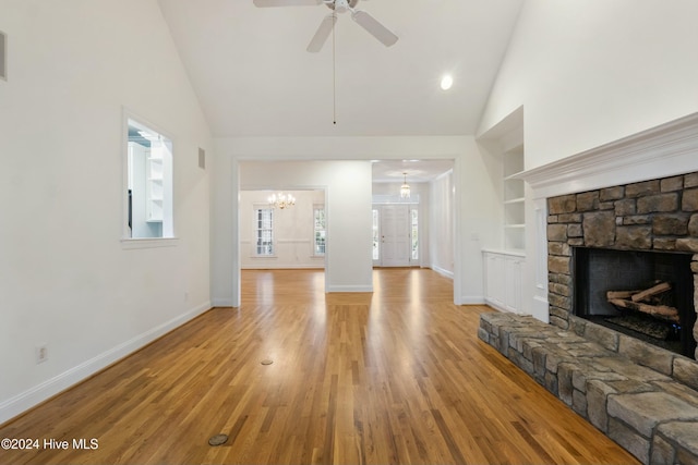 unfurnished living room with built in shelves, high vaulted ceiling, a fireplace, ceiling fan with notable chandelier, and light wood-type flooring