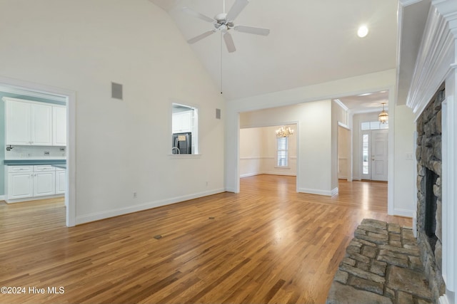 unfurnished living room featuring a fireplace, light hardwood / wood-style flooring, high vaulted ceiling, and ceiling fan with notable chandelier