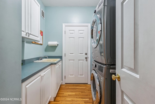 laundry room featuring stacked washer / dryer, sink, cabinets, and light hardwood / wood-style flooring