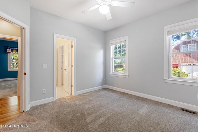 unfurnished bedroom featuring light colored carpet, ensuite bath, and ceiling fan