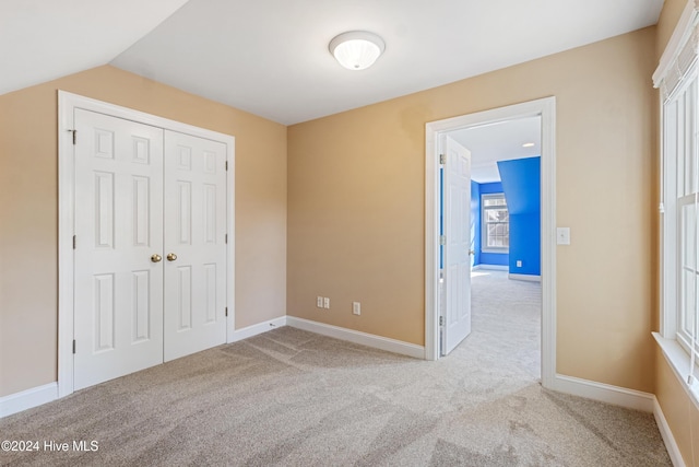 unfurnished bedroom featuring a closet, light colored carpet, and vaulted ceiling