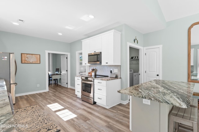 kitchen with light stone countertops, white cabinets, light hardwood / wood-style flooring, appliances with stainless steel finishes, and a kitchen bar