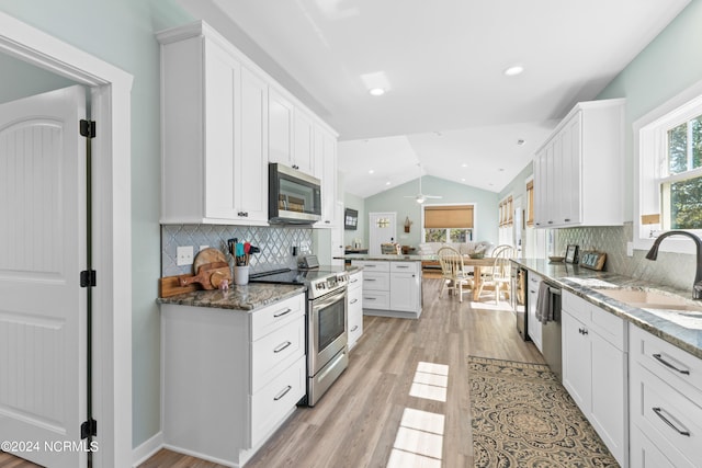 kitchen with appliances with stainless steel finishes, lofted ceiling, decorative backsplash, and white cabinets