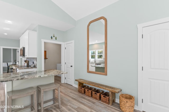 kitchen with white cabinets, light hardwood / wood-style flooring, a breakfast bar area, light stone countertops, and vaulted ceiling