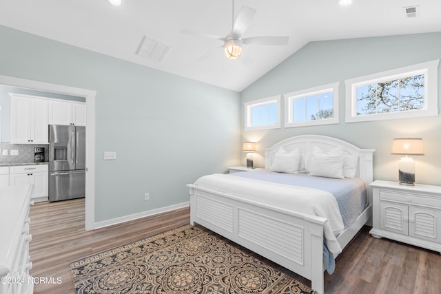 bedroom with stainless steel fridge, hardwood / wood-style flooring, ceiling fan, and vaulted ceiling