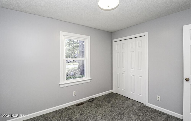 unfurnished bedroom with a textured ceiling, a closet, dark carpet, and multiple windows