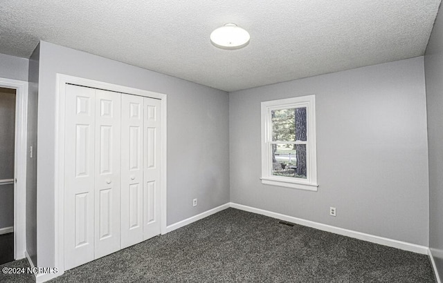 unfurnished bedroom with a textured ceiling, a closet, and dark carpet