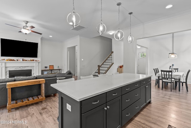 kitchen featuring a kitchen island, a premium fireplace, ornamental molding, pendant lighting, and light hardwood / wood-style floors