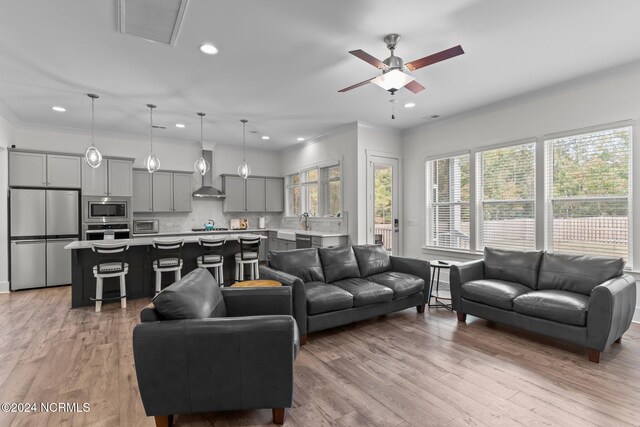 living room with light hardwood / wood-style floors, ornamental molding, and ceiling fan