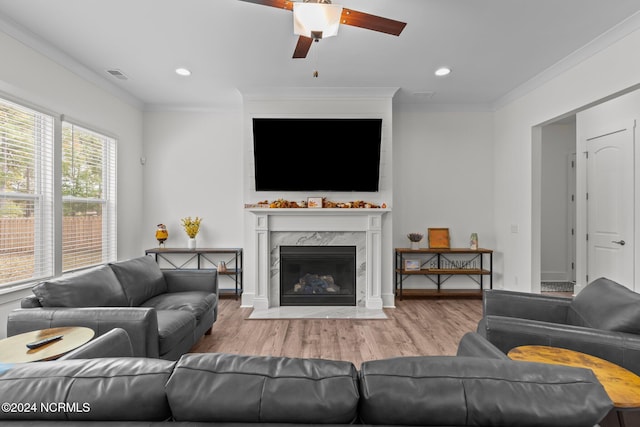 living room featuring crown molding, light wood-type flooring, a high end fireplace, and ceiling fan