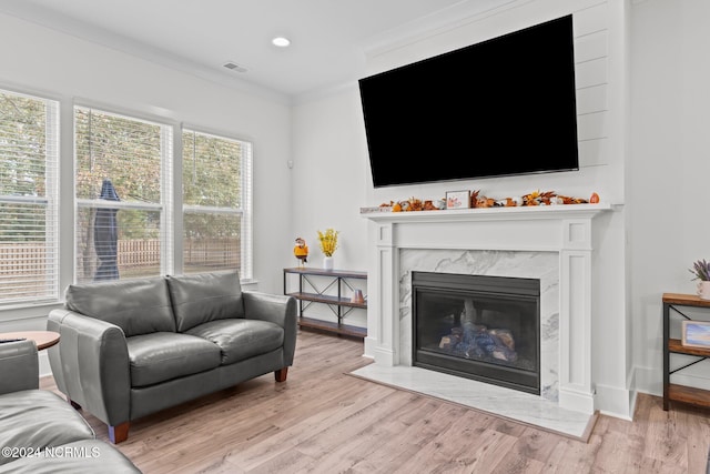 living room featuring a premium fireplace, crown molding, and light wood-type flooring