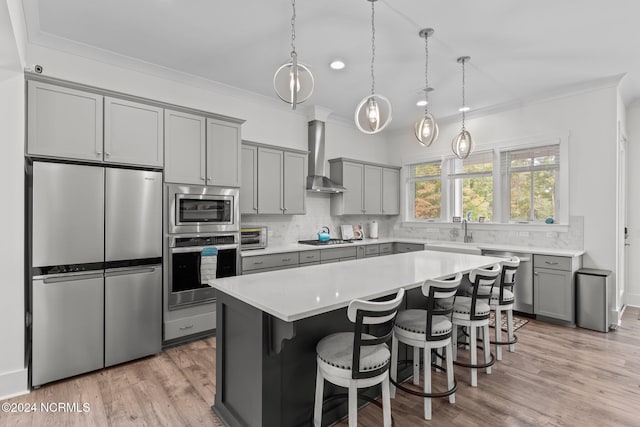 kitchen with wall chimney range hood, a breakfast bar area, light hardwood / wood-style flooring, stainless steel appliances, and a center island