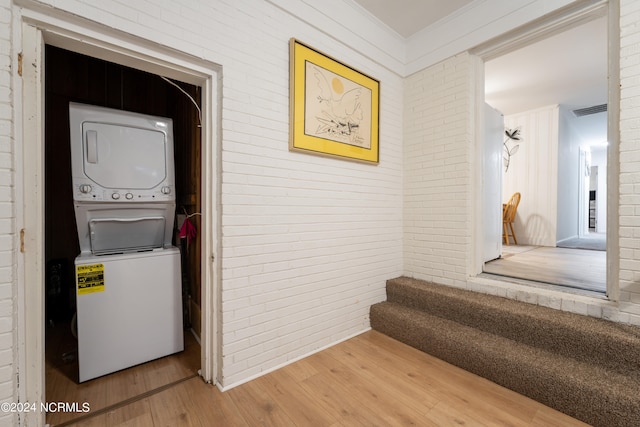 hall with brick wall, crown molding, stacked washer and dryer, and wood-type flooring