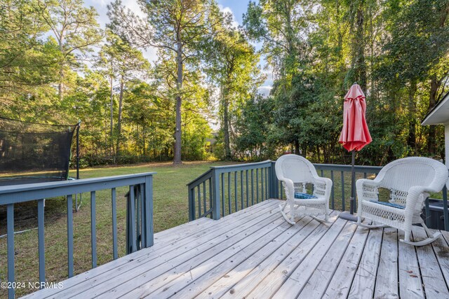 wooden deck featuring a trampoline and a lawn