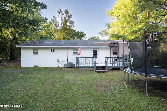 back of property featuring a wooden deck, a trampoline, a lawn, and central AC unit