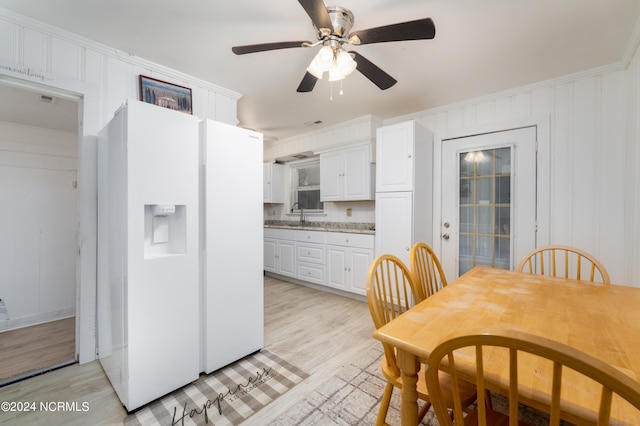 kitchen with white cabinets, ceiling fan, white fridge with ice dispenser, ornamental molding, and light hardwood / wood-style floors