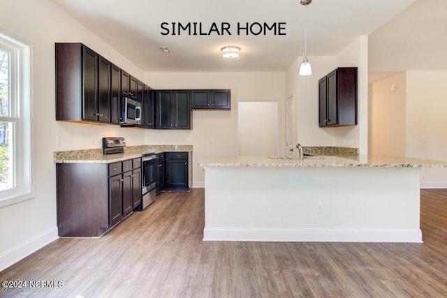 kitchen with light wood-type flooring, appliances with stainless steel finishes, decorative light fixtures, and a wealth of natural light