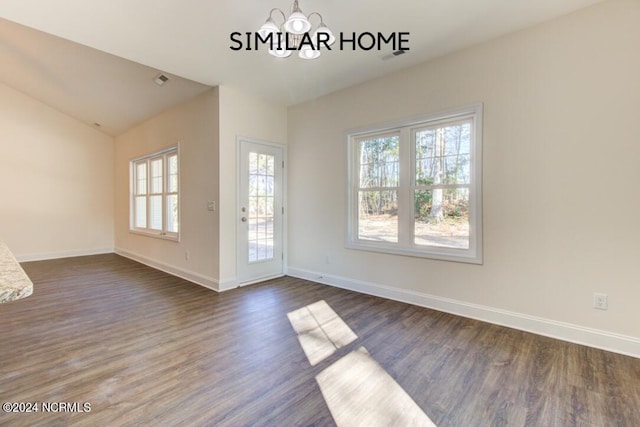 spare room featuring an inviting chandelier, dark wood-type flooring, vaulted ceiling, and a healthy amount of sunlight