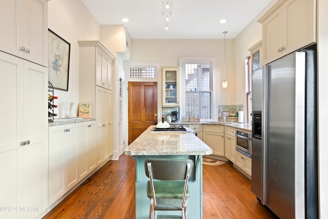 kitchen with light stone countertops, hanging light fixtures, stainless steel appliances, and dark hardwood / wood-style floors