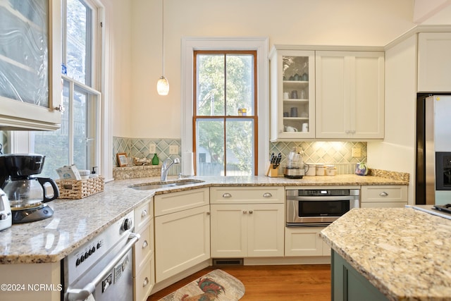 kitchen featuring white cabinets, light stone counters, light wood-type flooring, pendant lighting, and stainless steel appliances