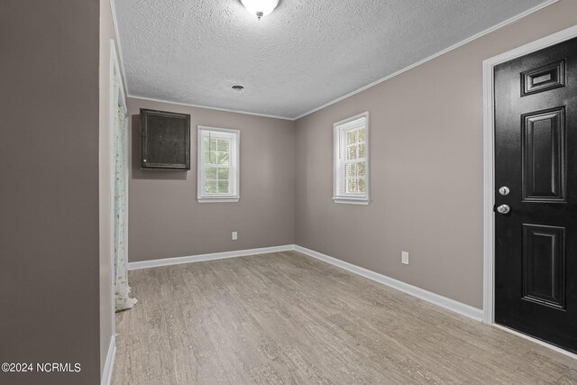 spare room featuring light hardwood / wood-style floors, crown molding, and a textured ceiling