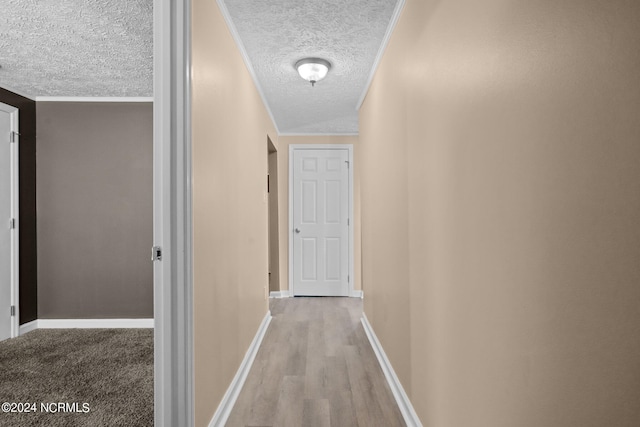 corridor featuring a textured ceiling, light wood-type flooring, and crown molding