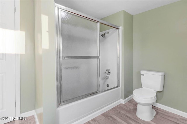 bathroom with toilet, wood-type flooring, and bath / shower combo with glass door