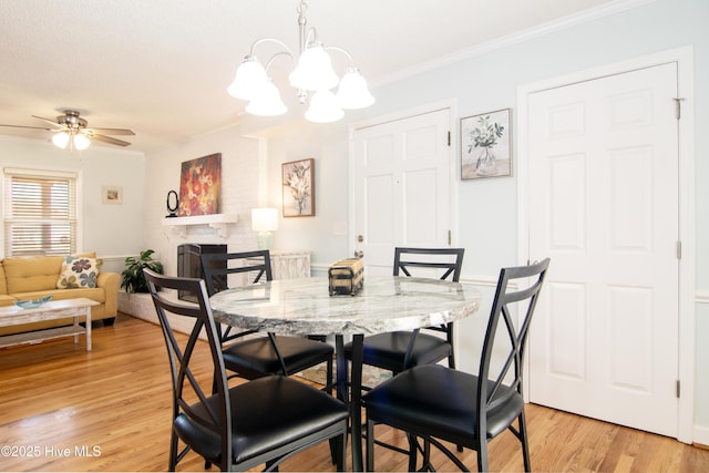 dining area featuring light wood-style flooring, ceiling fan with notable chandelier, a large fireplace, and ornamental molding