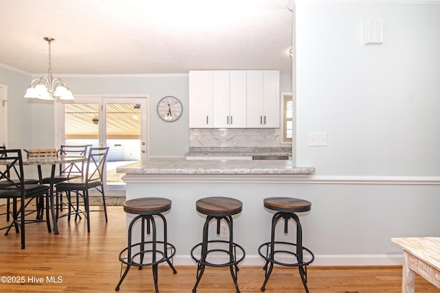 kitchen featuring light wood-type flooring, a kitchen breakfast bar, light countertops, and white cabinetry