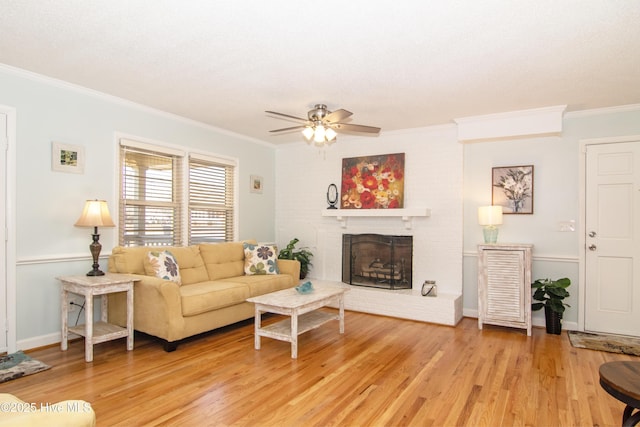 living area featuring light wood-type flooring, ornamental molding, a fireplace, baseboards, and ceiling fan