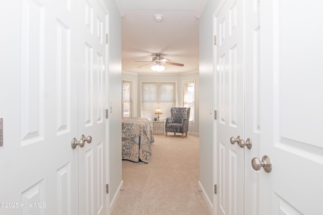 corridor with light colored carpet, crown molding, and baseboards