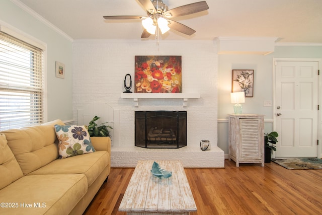 living area with a ceiling fan, wood finished floors, a fireplace, and ornamental molding