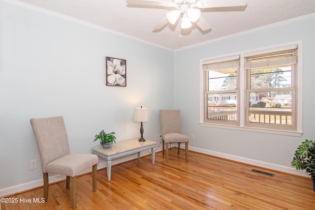 living area with light wood-type flooring, visible vents, crown molding, baseboards, and ceiling fan