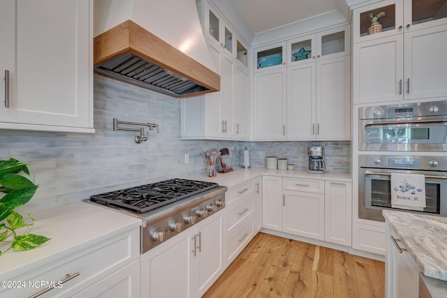 7 S Waterfront Pl, Hampstead, NC 28443 - kitchen featuring decorative backsplash, light wood-type flooring, premium range hood, stainless steel appliances, and white cabinetry
