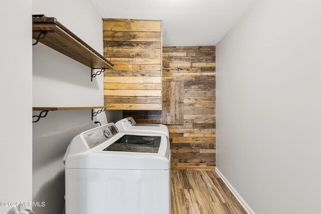 laundry room featuring light hardwood / wood-style floors, wood walls, and washer and dryer