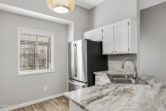 kitchen with light stone countertops, sink, light wood-type flooring, white cabinetry, and stainless steel refrigerator