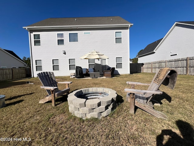 back of property with an outdoor fire pit and a yard