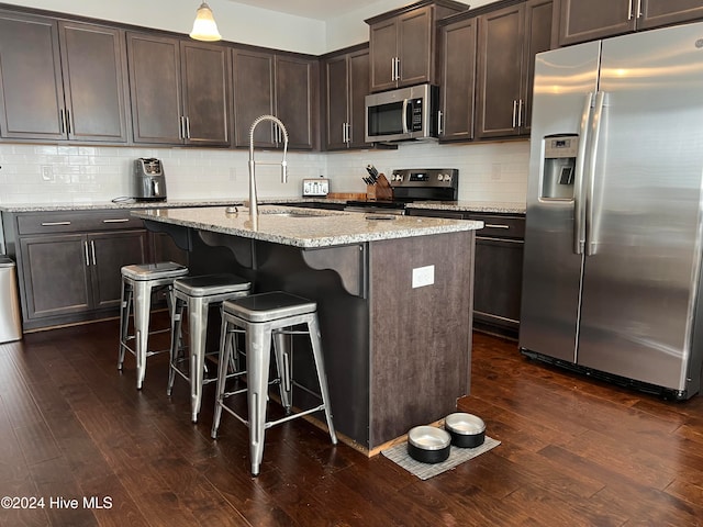 kitchen with a center island with sink, appliances with stainless steel finishes, dark hardwood / wood-style floors, and light stone countertops