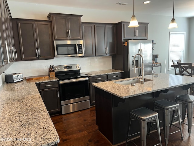 kitchen with a center island with sink, light stone countertops, appliances with stainless steel finishes, hanging light fixtures, and dark hardwood / wood-style floors