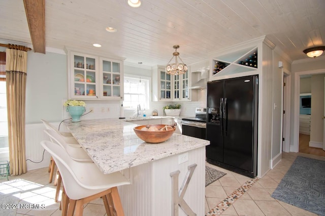 kitchen featuring a breakfast bar area, black fridge, decorative light fixtures, stainless steel range with electric cooktop, and wall chimney exhaust hood