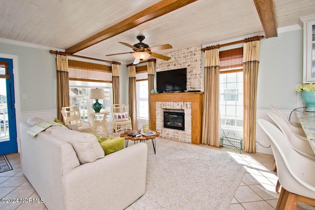 tiled living room featuring beamed ceiling, ornamental molding, ceiling fan, a brick fireplace, and wooden ceiling