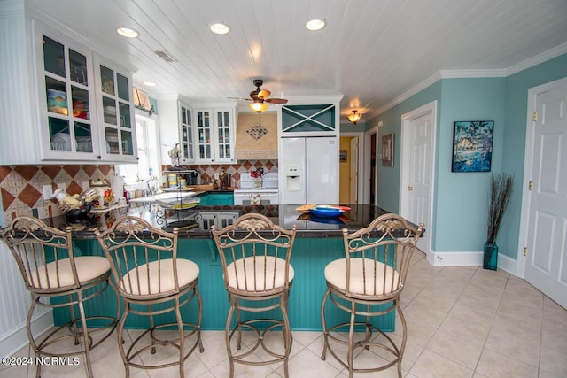 kitchen featuring a breakfast bar, tasteful backsplash, kitchen peninsula, white refrigerator with ice dispenser, and white cabinets