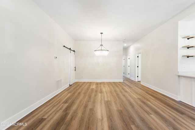 unfurnished room featuring a chandelier, a barn door, and light hardwood / wood-style flooring