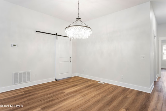 unfurnished dining area featuring hardwood / wood-style floors, a notable chandelier, and a barn door