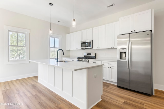 kitchen with appliances with stainless steel finishes, sink, light hardwood / wood-style flooring, white cabinets, and an island with sink