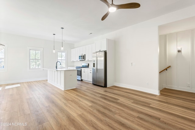 kitchen featuring appliances with stainless steel finishes, a center island with sink, decorative light fixtures, white cabinets, and light hardwood / wood-style floors