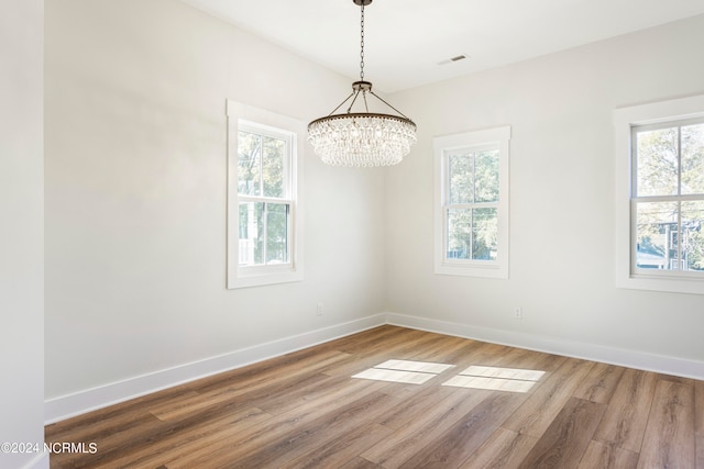 spare room featuring a wealth of natural light, wood-type flooring, and an inviting chandelier