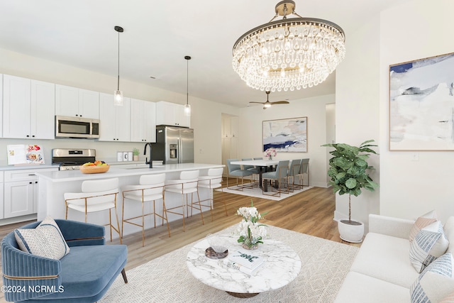 living room with ceiling fan with notable chandelier, light wood-type flooring, and sink