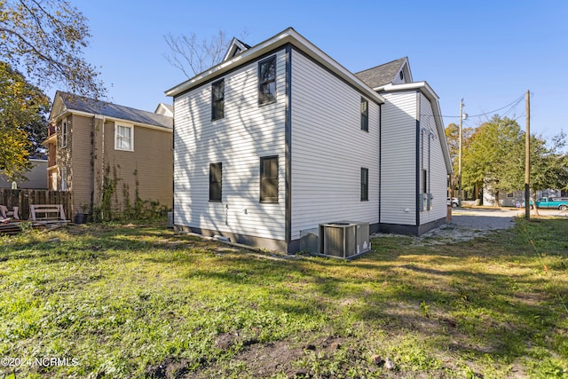 rear view of house with central AC unit and a yard